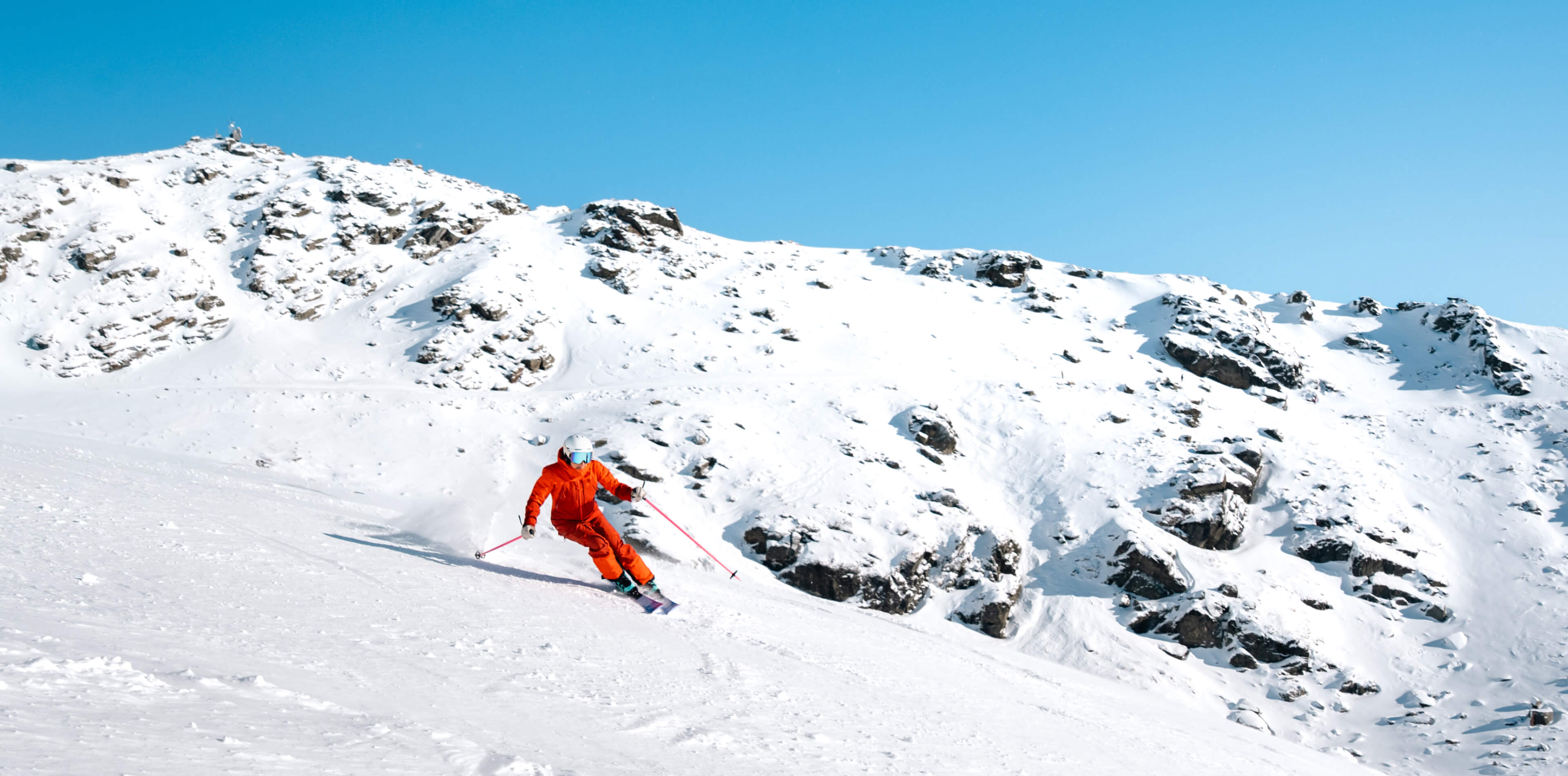 Skier descending down a snowy Remarkables mountain slope under a clear blue sky.